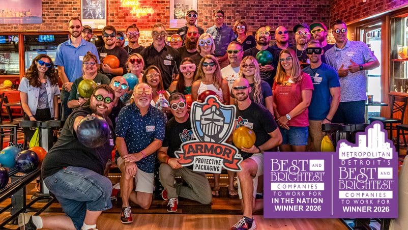 ARMOR Group Photo of employees standing with silly glasses at a bowling ally behind a Best and Brightest Companies to Work for in the Nation and Metro Detroit's Best and Brightest Companies to Work For Sign