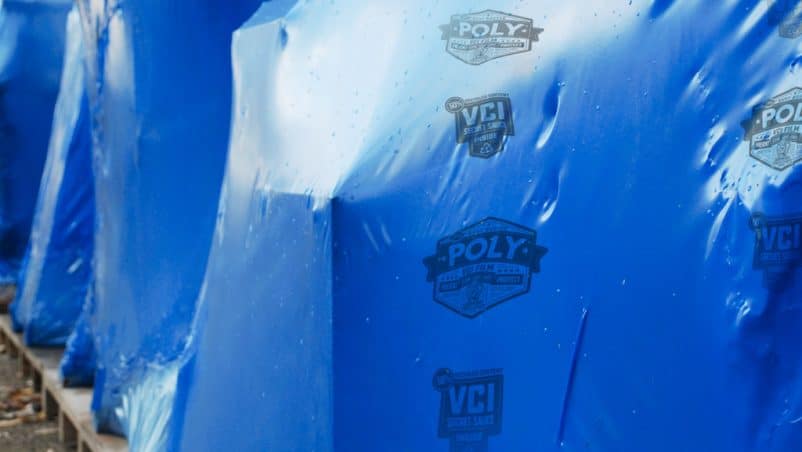 Large industrial items wrapped in ARMOR POLY® VCI Film labeled with 'POLY' and 'VCI', placed on wooden pallets for protection during storage or transport