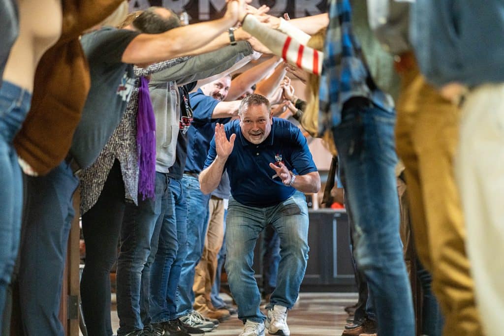 Armor protective packaging team meeting, man running through a tunnel formed by ARMOR employees